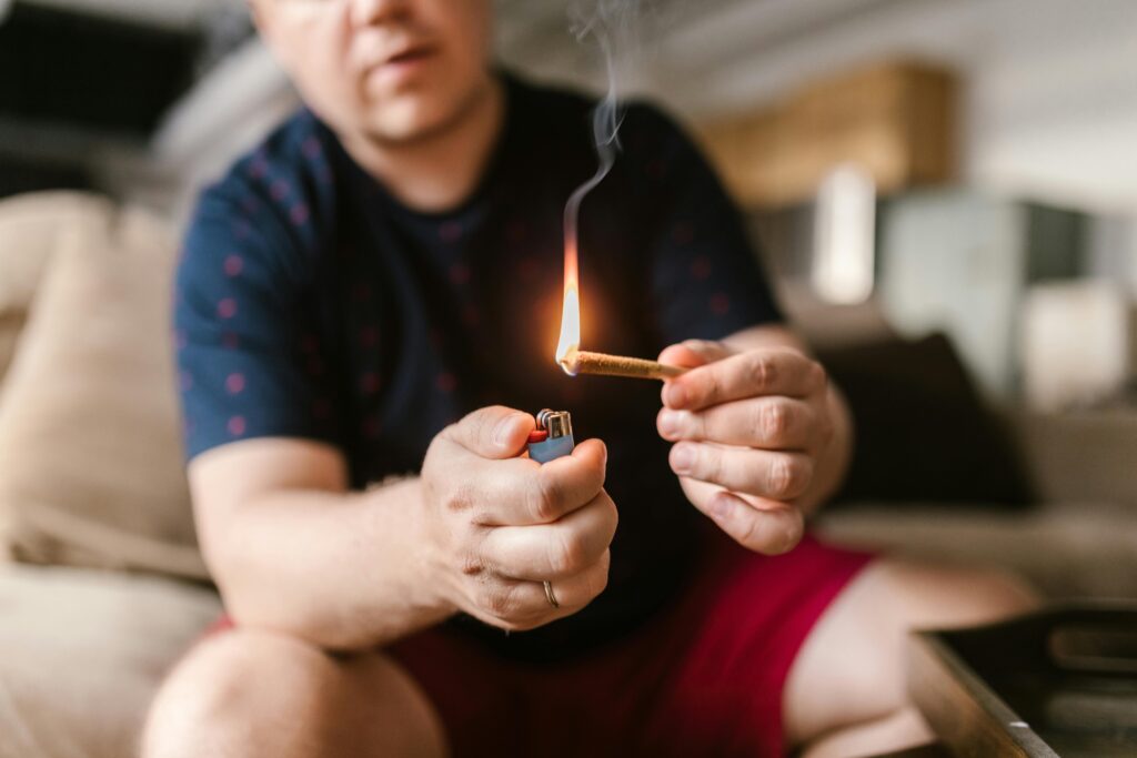 A person lighting a cannabis joint with a lighter, sitting indoors, showing hands closely.